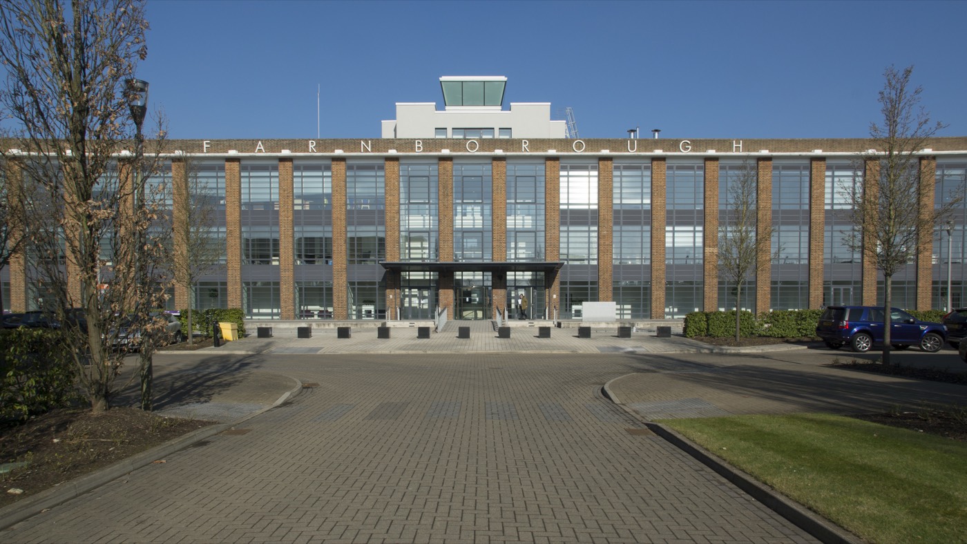 A large brick and glass office building behind a paved forecourt